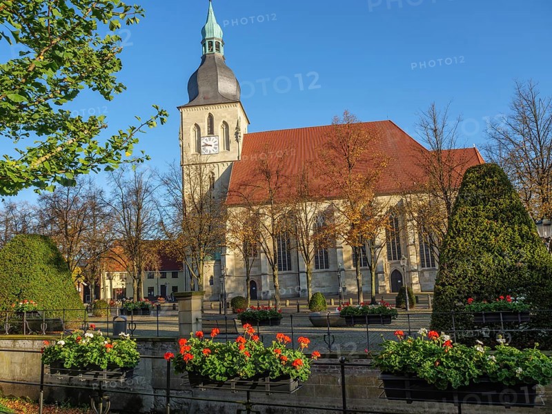 A historic church with a striking church tower, surrounded by blossoming flowers and autumnal trees under a blue sky, nottuln, münsterland, germany