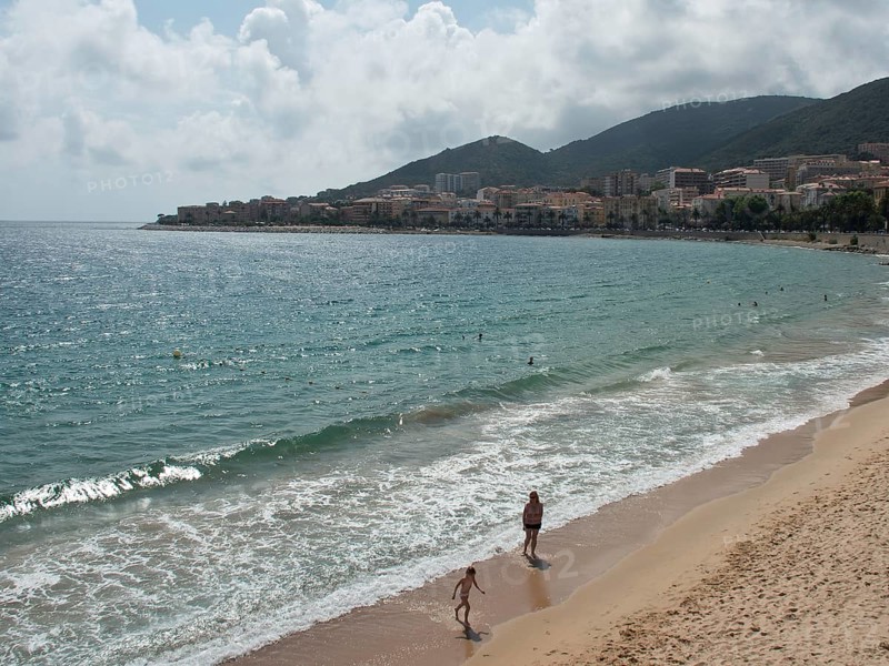 People walking along a sandy beach with a coastal town in the background, ajaccio, corsica, france