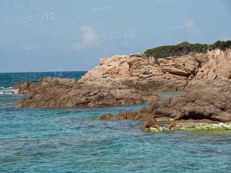 Rough rocky coast lapped by turquoise sea under a slightly cloudy sky, ajaccio, corsica, france