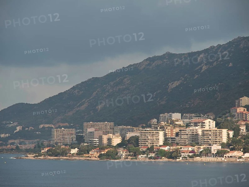 City on the coast with mountains in the background, partly cloudy sky and many buildings along the water, ajaccio, corsica, france