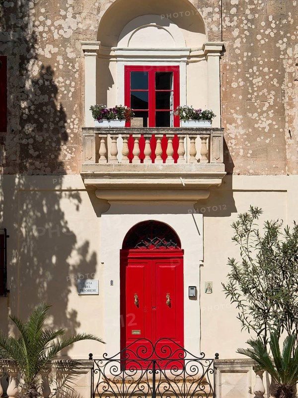 Charming building with bright red windows and doors and a small balcony with flowers, mdina, mediterranean sea, malta