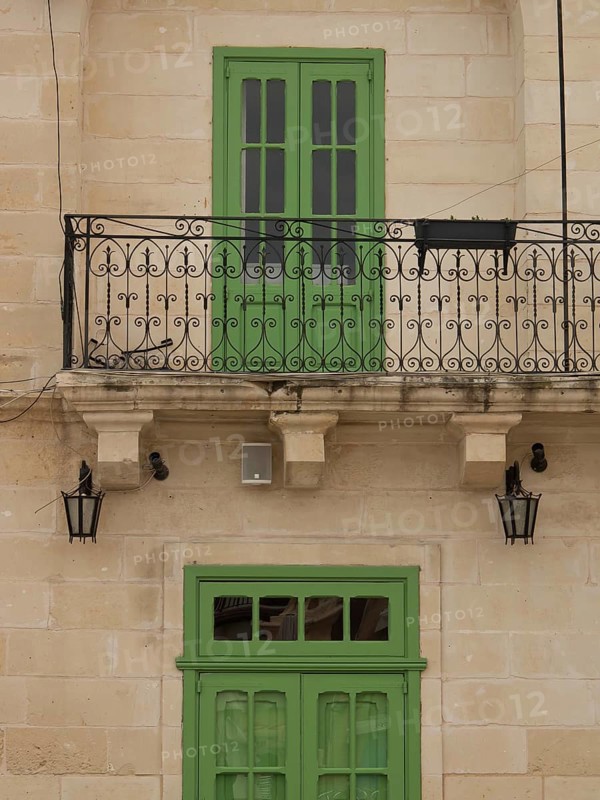 A green balcony with decorative lattice on a yellowish building, marsaxlokk, mediterranean sea, malta