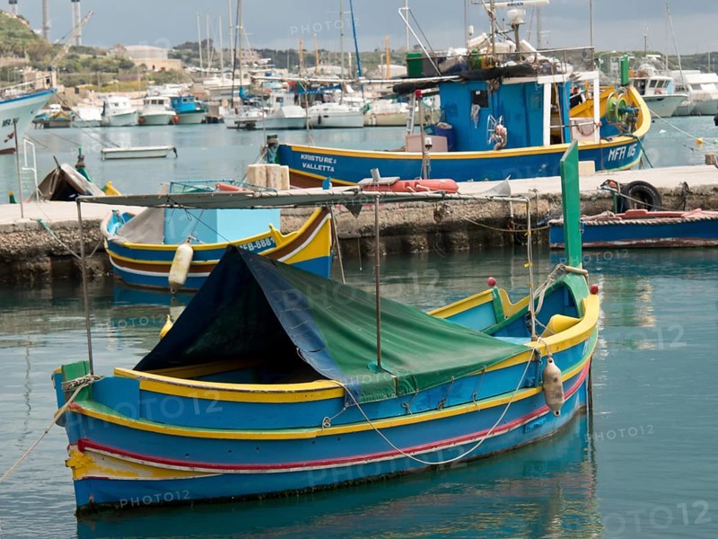 A blue and yellow fishing boat lies calmly in the water of a harbour, marsaxlokk, mediterranean sea, malta
