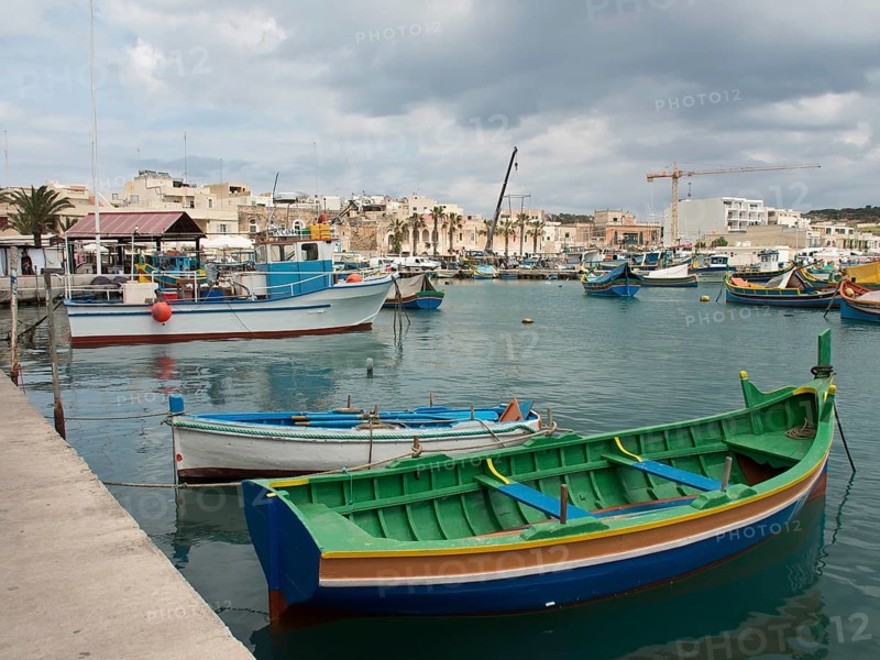Colourful boats in the harbour overlooking a small town, under a cloudy sky, marsaxlokk, mediterranean sea, malta
