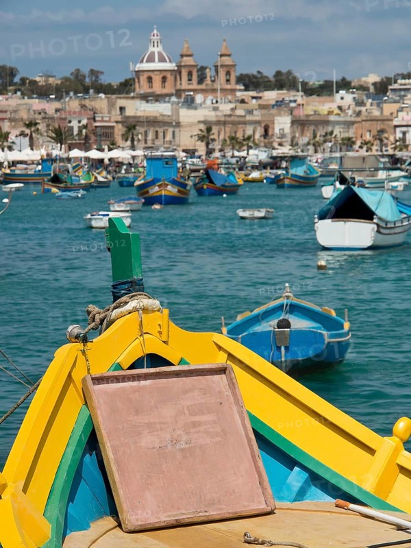View from the bow of a boat of a harbour town with several boats in the water, marsaxlokk, mediterranean sea, malta