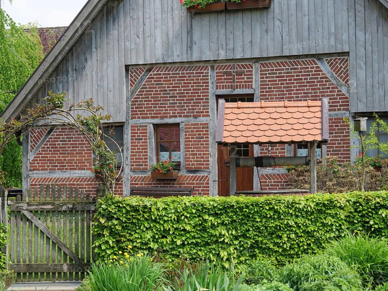 A traditional half-timbered house with red brick and wooden elements, framed by a well-tended garden, marbeck, westphalia, germany