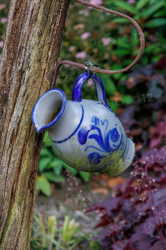 Close-up of a blue and white decorative jug hanging from a wooden post in a flowery garden, Borken, Münsterland, North Rhine-Westphalia, Germany, Europe