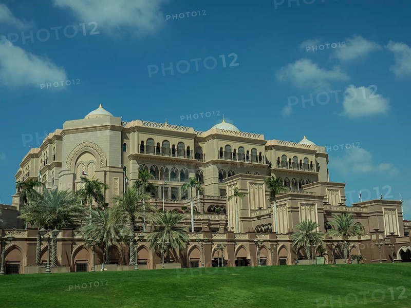 Magnificent palace with palm trees and green lawn under a clear sky, abu dhabi, united arab emirates
