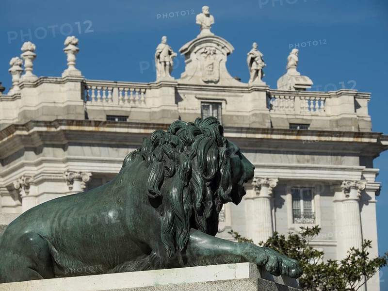 Bronze lion statue in front of a magnificent building with several stone figures under a clear sky, Madrid, Spain, Europe