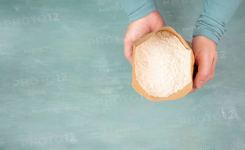 Baker holds paper bag with white wheat flour, baking ingredient for bread, pizza or pastry