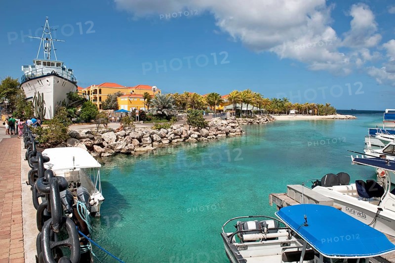 View of shallow inlet between small islands through lagoon in the background orange-coloured buildings of Royal Sea Aquarium Resort, on the left at the edge of the picture on land small island accessible via short bridge installed on dry land placed ship at the entrance entrance area of Sea Aquarium maritime museum, Caribbean, Windward Islands, Netherlands Antilles, ABC Islands ABC Islands, Willemstad, Curaçao Curacao