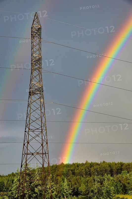 Double rainbow behind a high-voltage pylon, young cedars in the foreground, France, Europe
