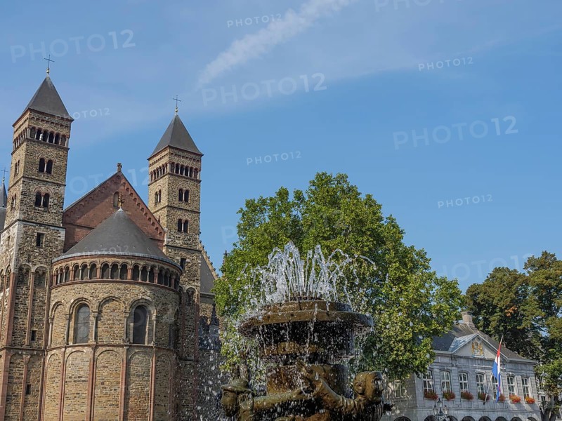 A fountain bubbles in front of a historic church building with two towers, Maastricht, limburg, netherlands