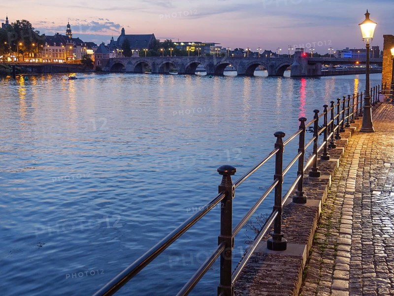 Evening riverside promenade with river and illuminated street lamp and reflective lights, Maastricht, limburg, netherlands