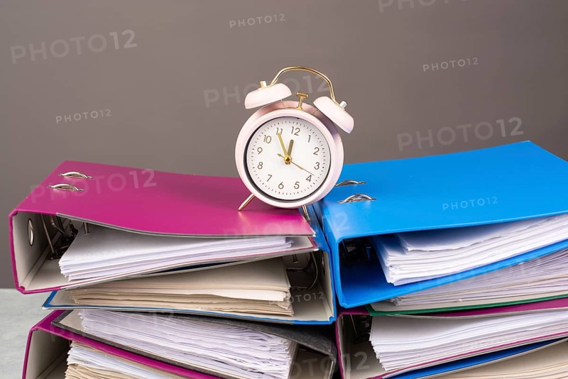 Alarm clock standing on pile of file folders, burnout, stress and overworked, pressure at work, deadline