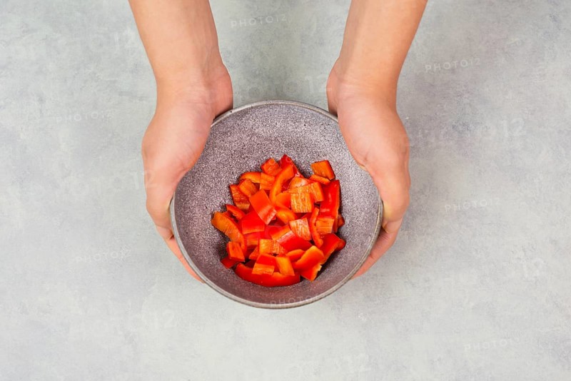 Tomatoes and red sliced pepper pieces in a bowl, prepare healthy food with paprika vegetables, holding fresh organic nutrition in the hands