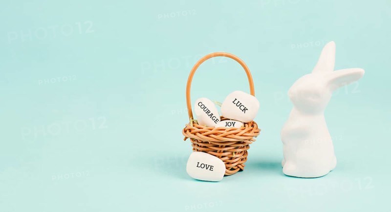 Easter bunny or rabbit with wicker basket, words like love, luck, joy and courage are standing on pebbles, gift and wishes for holiday