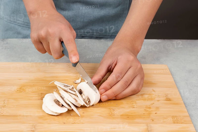 Cutting champignon mushrooms on a wooden board, prepare salad, healthy food with vegetables, fresh organic nutrition, cooking ingredients