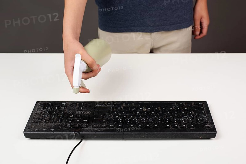 Cleaning computer keyboard in office, spraying water with a spray bottle dusty and dirty electronic, housework