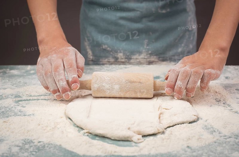 Baker rolls out dough for pizza, flatbread or pastry with rolling pin, prepare ingredients for food, baking for holidays
