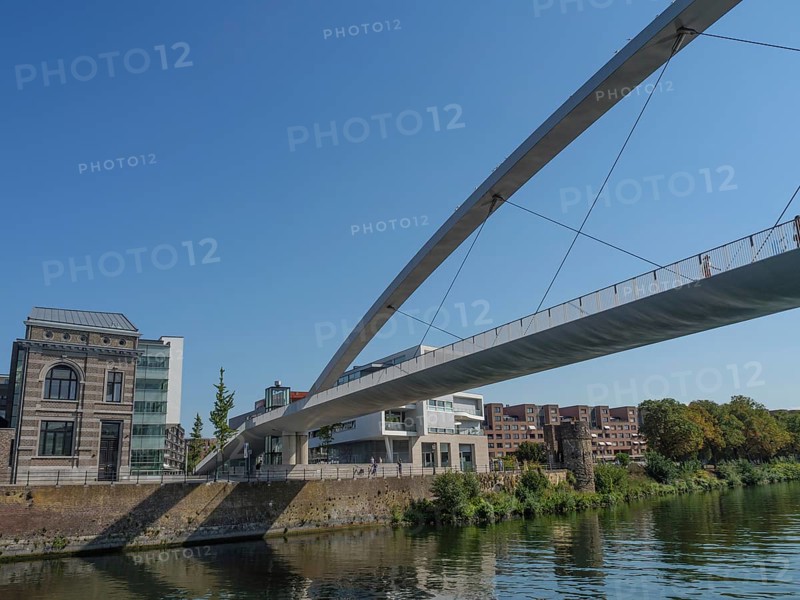 View of a modern bridge over a river with neighbouring urban buildings and blue sky, Maastricht, limburg, the netherlands