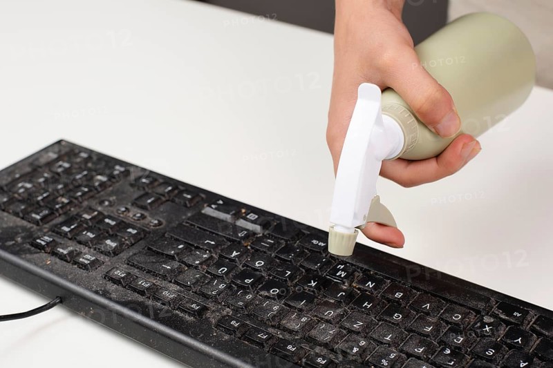 Cleaning computer keyboard in office, spraying water with a spray bottle dusty and dirty electronic, housework