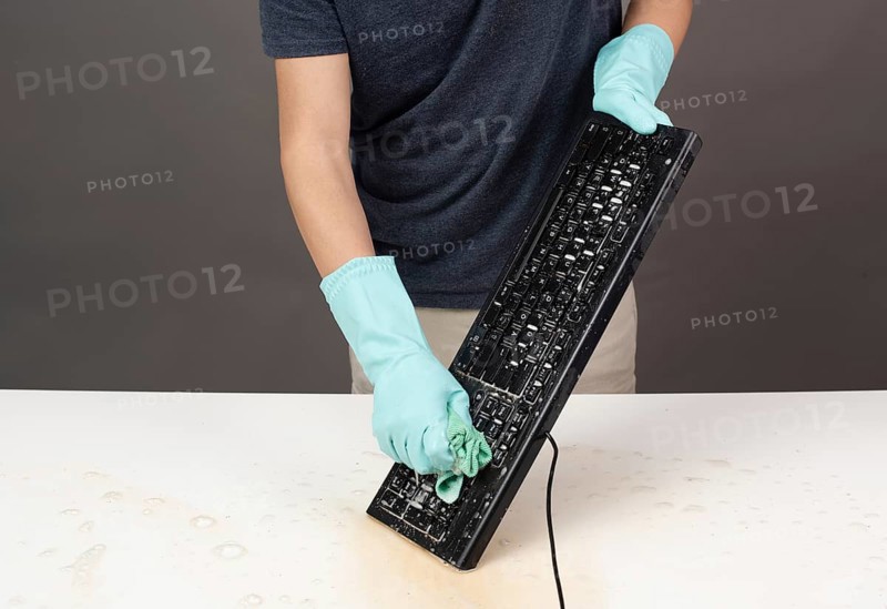 Cleaning computer keyboard in office with rubber protective glove, whiping with water and soap, cleaning dusty and dirty electronic, housework