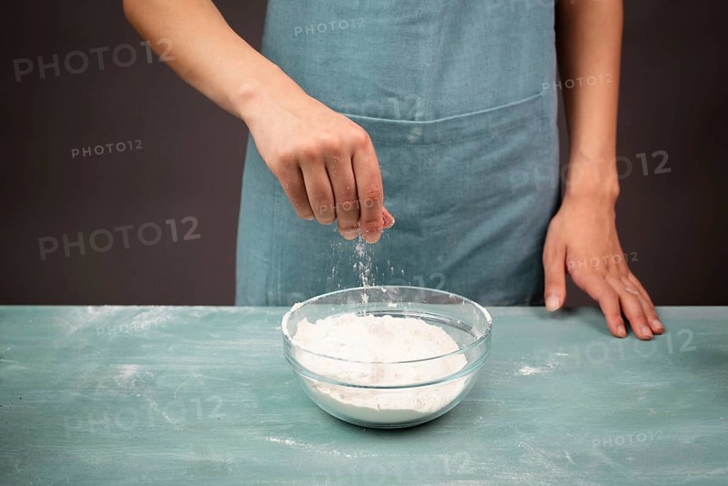 Baker sprinkles salt into a bowl with flour, prepare dough for artisan bread or pizza, ingredients for food, baking pastry