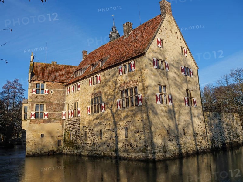An old moated castle with red shutters and a red roof, surrounded by water, lüdinghausen, westphalia, germany