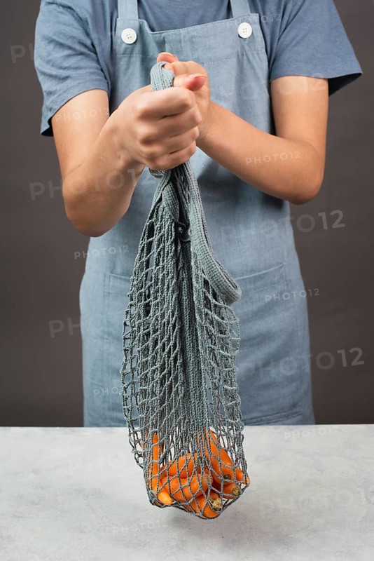 Holding fresh carrots in a reusable grocery mesh bag, vegetables from the market, healthy food and zero waste