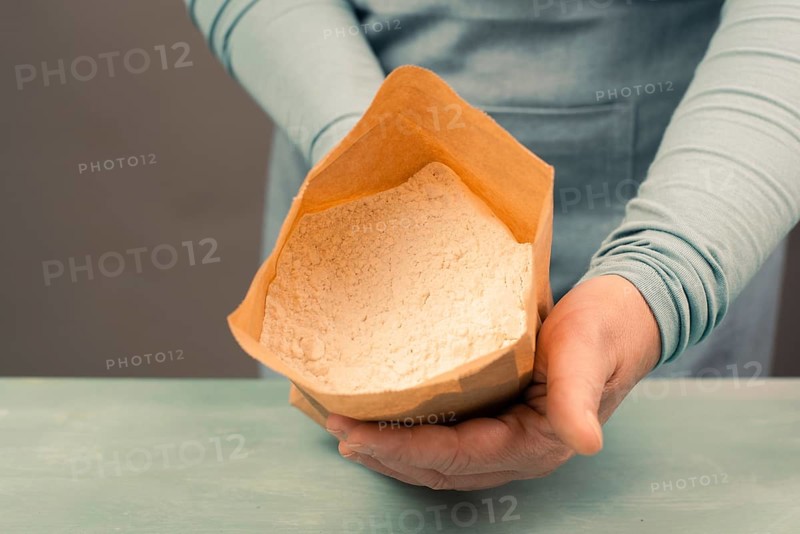 Baker holds paper bag with white wheat flour, baking ingredient for bread, pizza or pastry