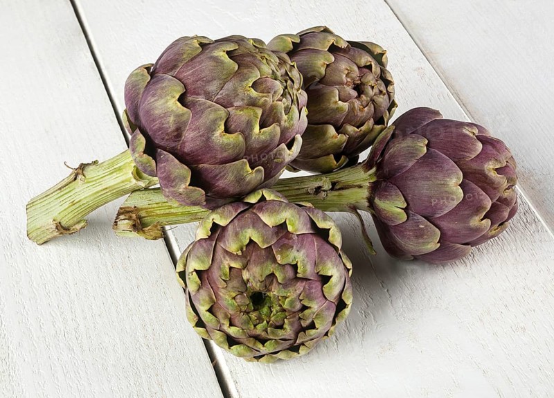 Four biological raw artichokes on white wooden table