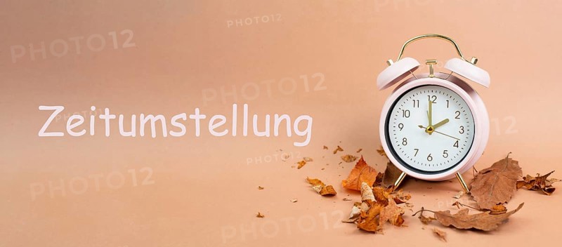Alarm clock with autumn foliage, end of daylight saving time in fall, winter time changeover stands in german language beside the clock