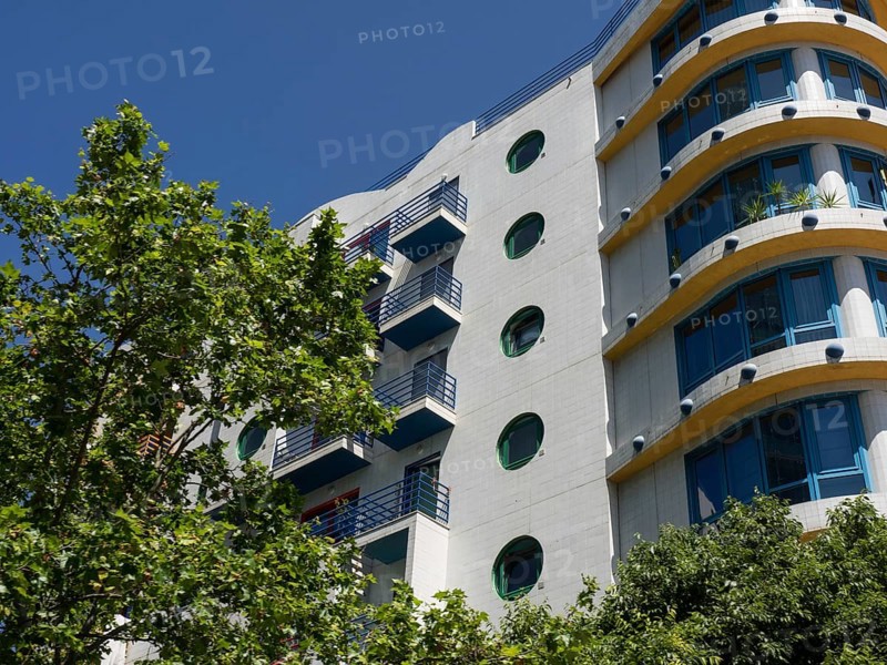 Modern residential building with round windows and balconies, green tree in the foreground, Lisbon, portugal