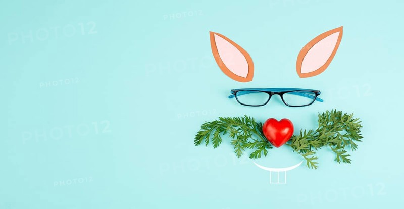 Easter rabbit face with a heart shaped nose, whiskers from carrot leaves and eyeglasse, holiday greeting card, spring season