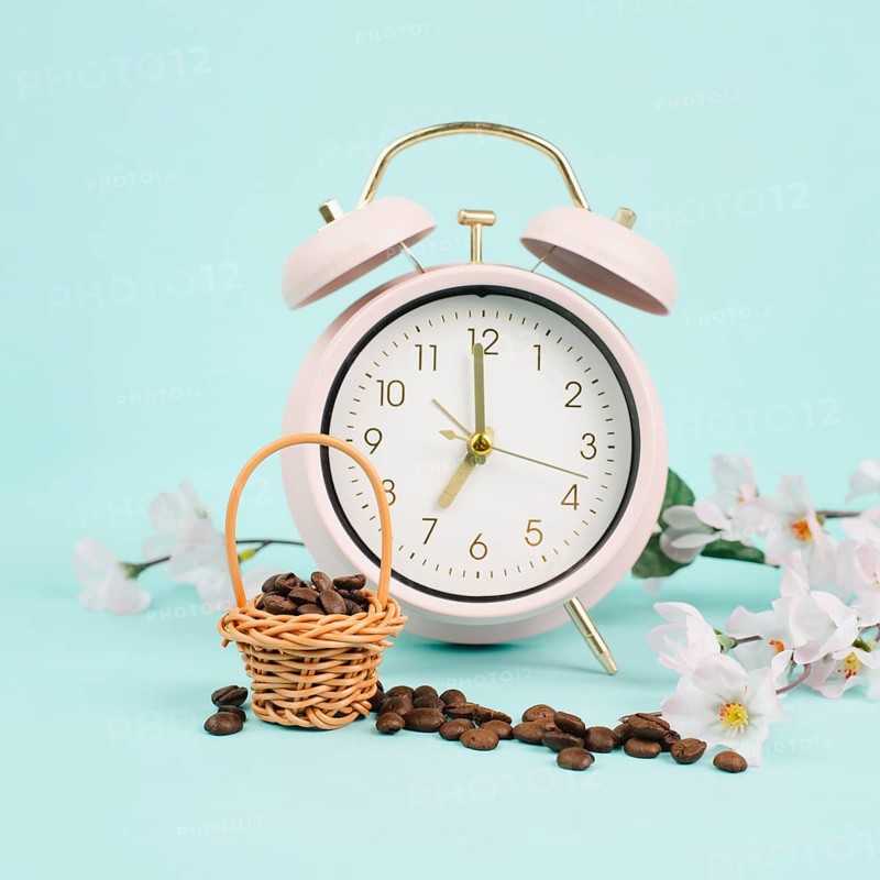 Wicker basket with roasted coffee beans, an alarm clock and cherry blossom, wake up in the morning, spring season