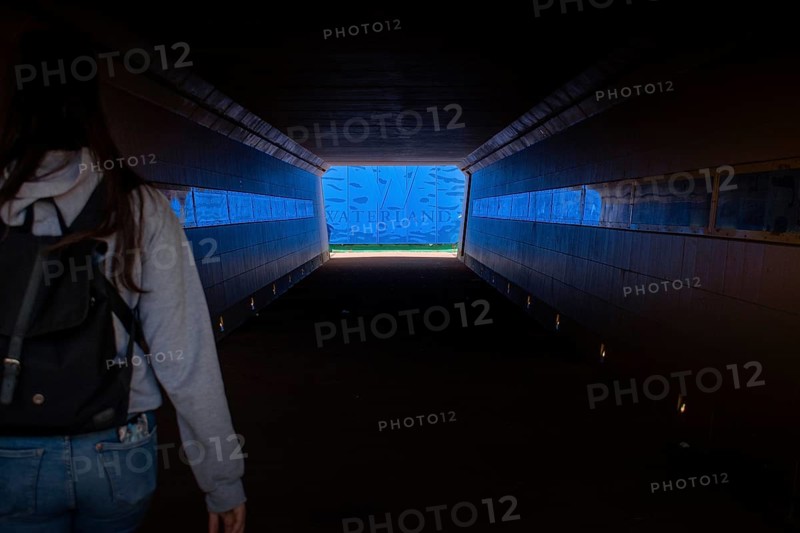 A woman in a dark tunnel walks towards a bright blue exit labelled Waterland, Ilpendam, Netherlands