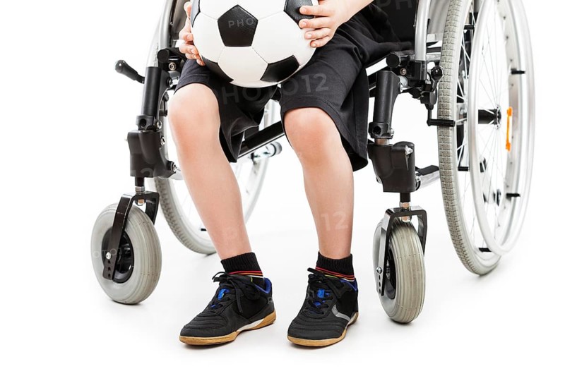 Invalid or disabled child boy sitting on wheelchair hand holding soccer sport ball white isolated