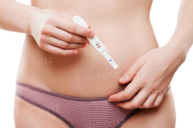 Beauty young woman with slim naked body shape wearing bikini panties hand holding pregnancy test showing two stripes positive result white isolated