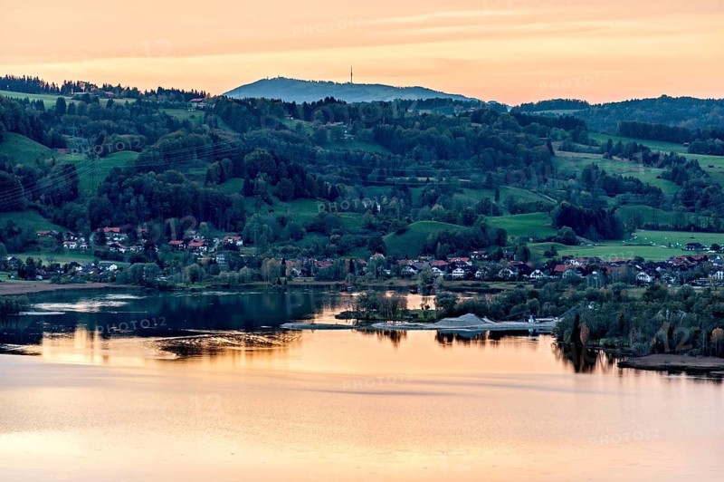 View of the Lake Kochel calm water, warm evening light, sunset, sand and gravel works Schlehdorf, Bromberg, behind Hoher Peissenberg, Bavarian Prealps, Alps, Upper Bavaria, Bavaria, Germany, Europe