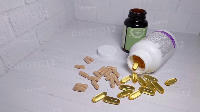 Scattered pills and capsules near two bottles on a white table against a brick wall