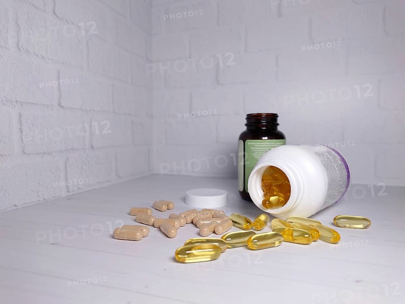 Opened supplement bottles with scattered pills and capsules on a white brick wall background