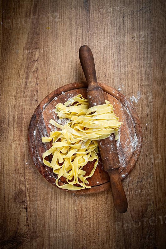 Raw tagliatelle pasta, homemade, on a rolling pin, top view, on a cutting board, cooking concept