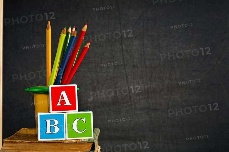 ABC and multicolored pencil on old textbook against blackboard in class. School concept