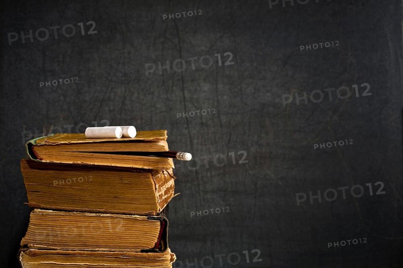 Chalk and pencil on old textbook against blackboard in class. School concept