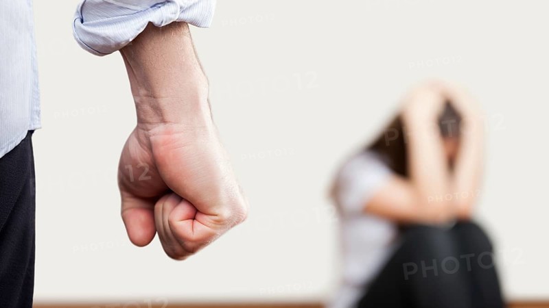Family violence and aggression concept, furious angry man raised punishment fist over scared or terrified woman sitting at wall corner