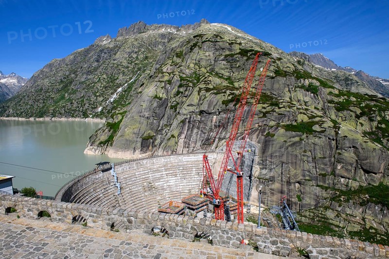 View from Grimsel Hospice Grimselhospiz to construction site of new dam for enlargement of reservoir Grimselsee replacement dam Spitallamm on the Grimsel in the Bernese Oberland, left old dam next to Grimsel Hospice Grimselhospiz, right two big red cranes, Guttanen, Canton Bern, Switzerland, Europe