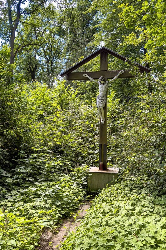 Old roofed cross with figure of Jesus Christ crucified on the cross at the edge of the forest, Germany, Europe