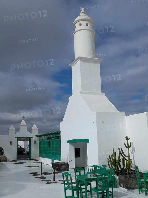 White lighthouse with buildings, green chairs and tables under a cloudy sky in Lanzarote, arrecife, Lanzarote, Canary Islands, Spain, Europe