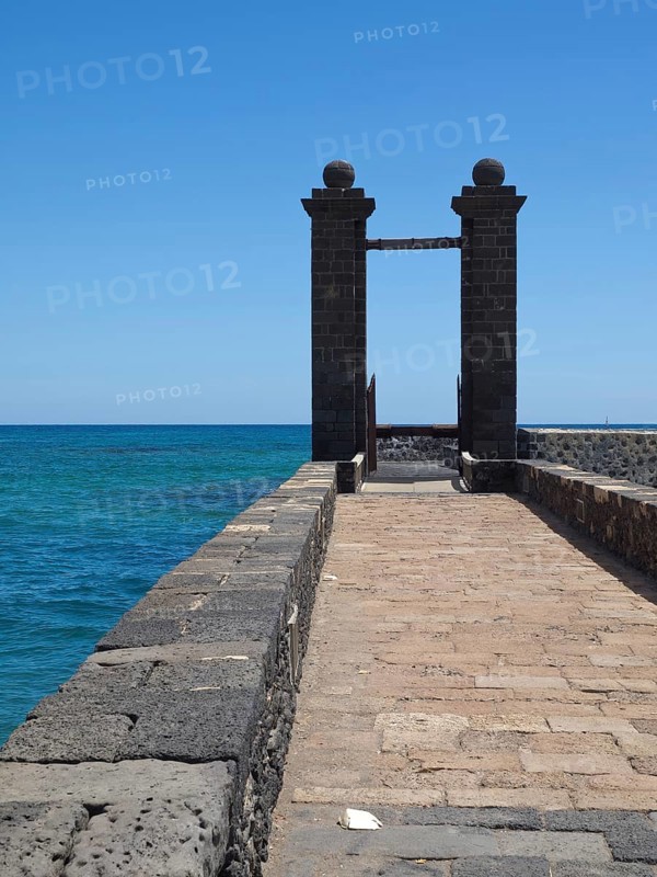 A stone footbridge leads to a Tor tor with a view of the blue sea and sky, arrecife, Lanzarote, Canary Islands, Spain, Europe